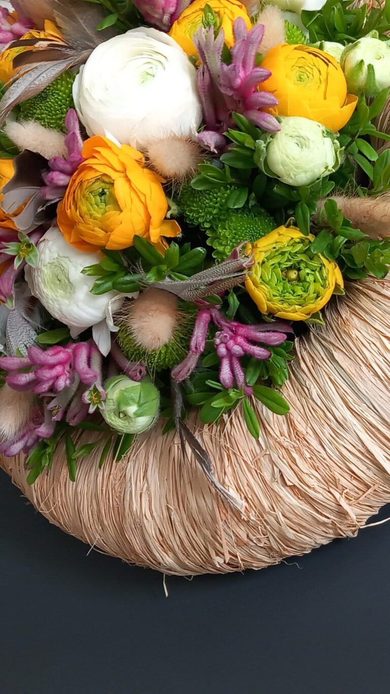 Detail van een lentekrans met witte en oranje ranonkels, hyacint en veren op een gevlochten basis