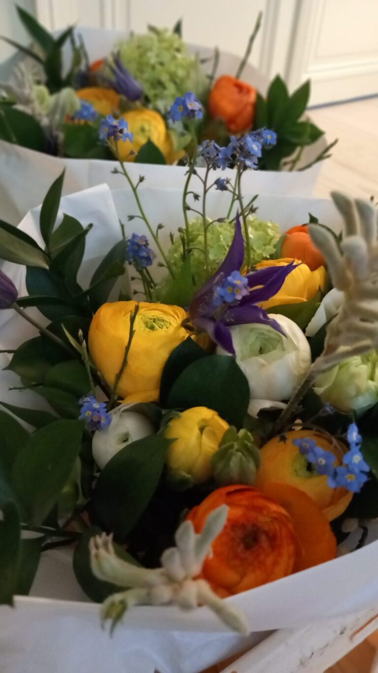 Kleurrijk lenteboeket met gele en oranje ranonkels en blauwe voorjaarsbloemen, ingepakt in papier