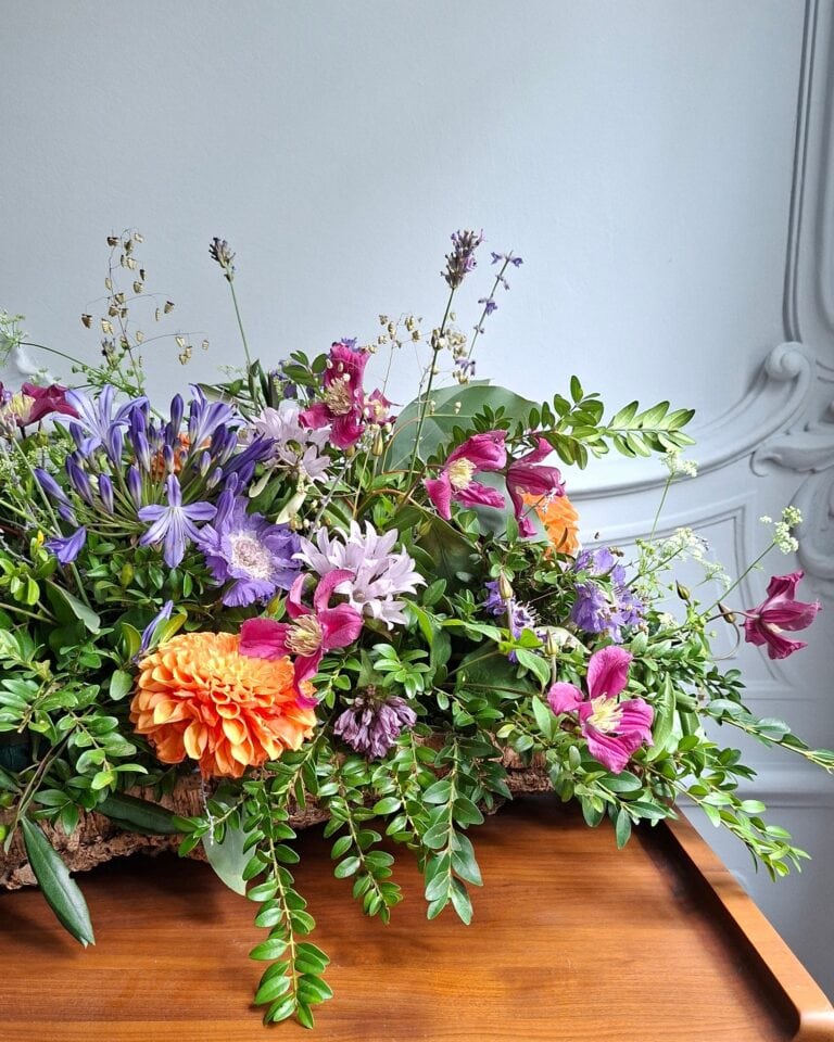 Laag langwerpig bloemstuk met agapanthus, clematis en een oranje dahlia op een houten tafel