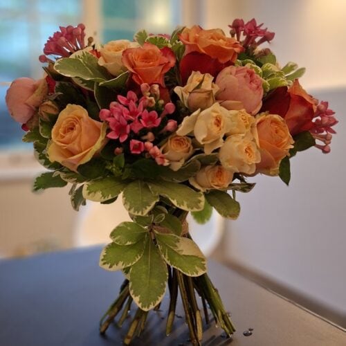 Handgebonden rozenboeket in zalm, crème en oranje met roze bouvardia en bont blad.