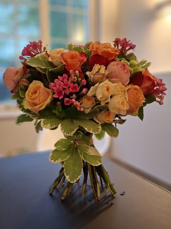 Handgebonden rozenboeket in zalm, crème en oranje met roze bouvardia en bont blad.