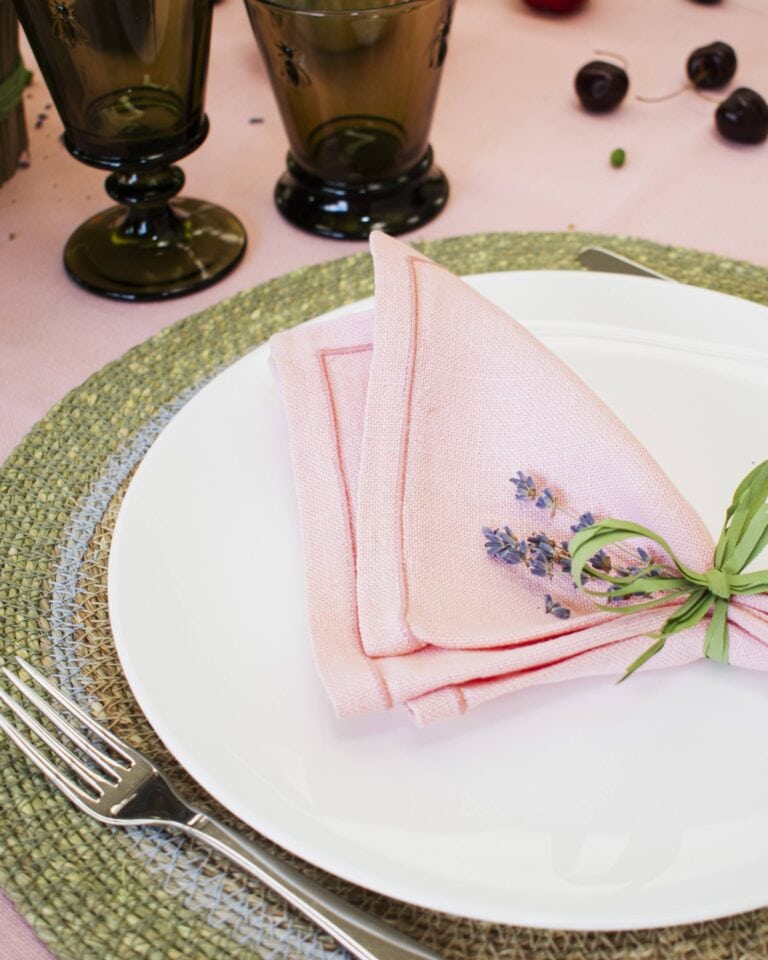 Roze linnen servet met een takje lavendel, gebonden op een wit bord met een gevlochten placemat
